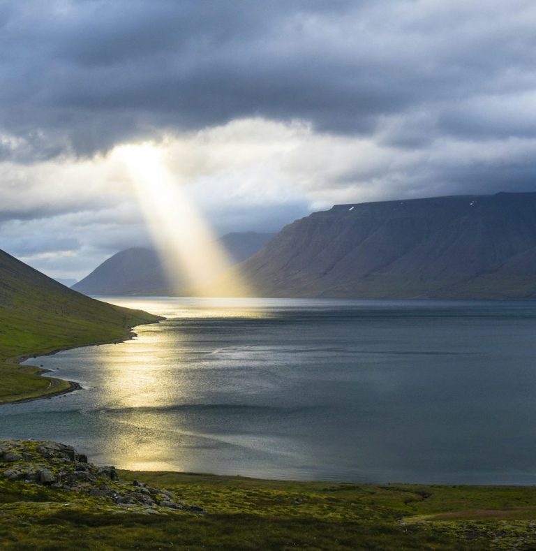 Sunbeam through Storm Clouds Dramatic sunbeam breaking through storm clouds over mountain lake landscape.